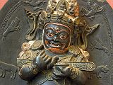 British Museum Top 20 Buddhism 13 Mahakala 13. Mahakala  Tibet, 17C AD. This stone stele shows the dharmapala (protective figure) Mahakala as Lord of the Tent, an appropriate role given the nomadic lifestyle of many Tibetans. The garland of skulls, his fierce expression and the prone male figure being trampled underfoot all add to his terrifying appearance. These symbolize his ability to destroy all impediments to enlightenment. Mahakala holds in the crooks of his arms the long wooden sounding board used to summon monks to assembly.  The half-bird, half-man figure of the Hindu deity Garuda is shown alongside Mahakala. In Mahakala's head-dress is his parent Buddha, Akshobhya, the Tathagata Meditation Buddha of the East.